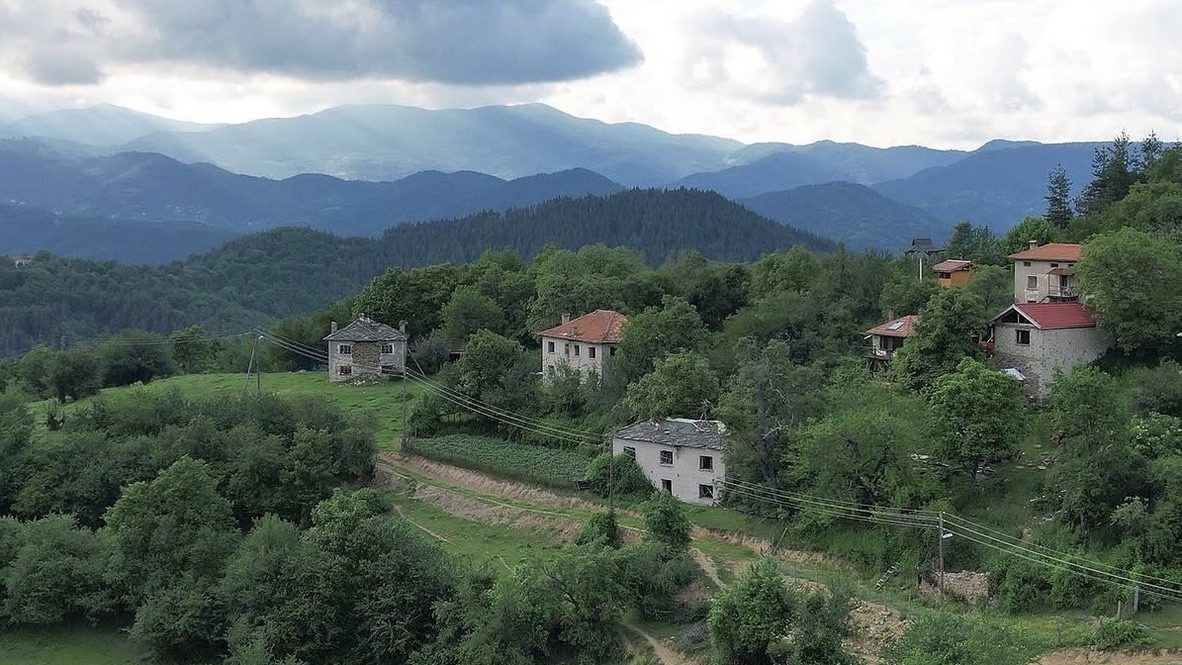 Stone houses on a green Rhodope slope under a heavy sky