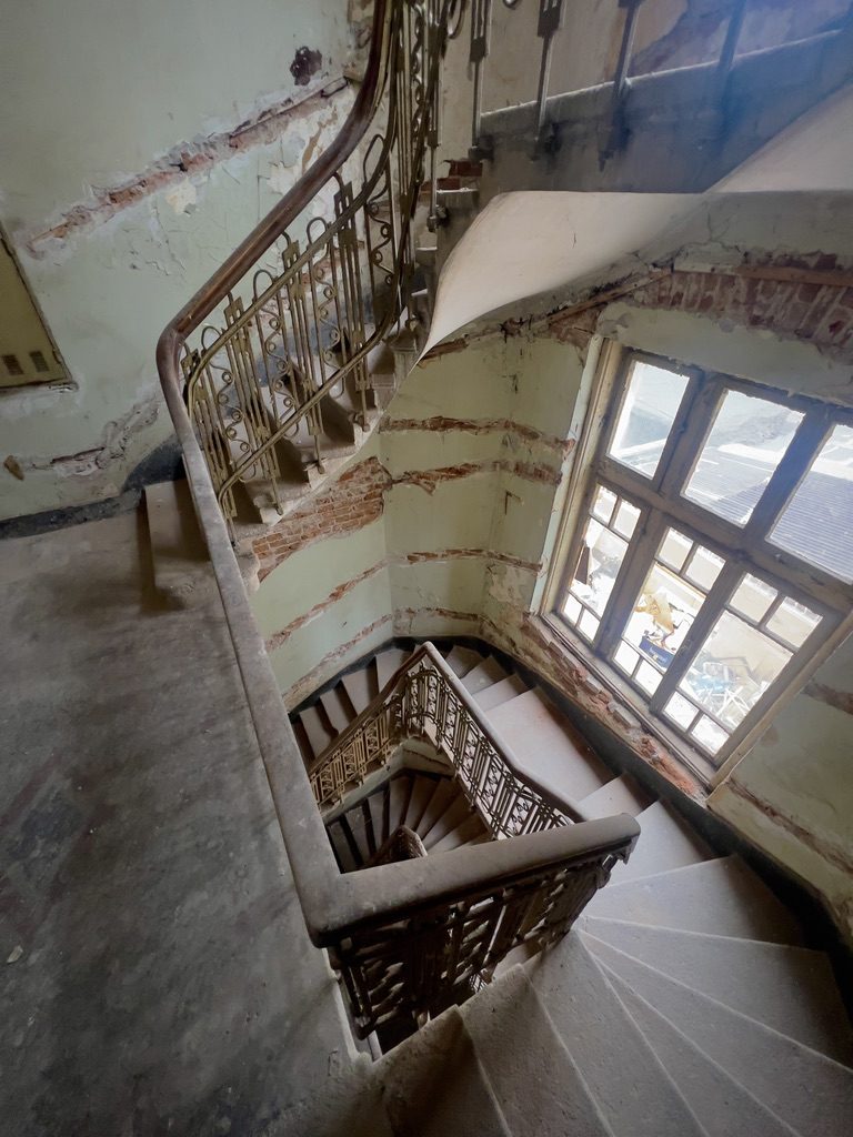 A spiral staircase with an ornate iron railing, plaster peeling from the walls