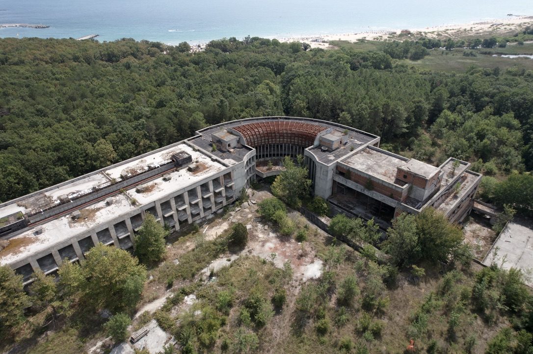 A curved concrete complex in the forest above a sandy beach