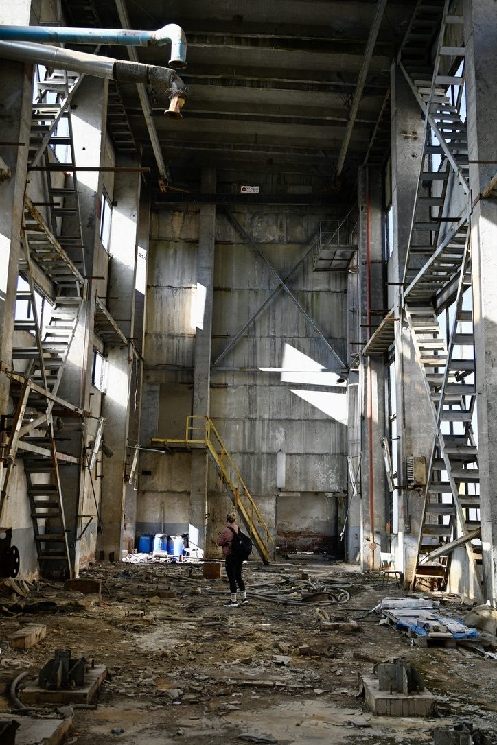 An explorer standing in a vast, empty factory hall lined with steel stairs