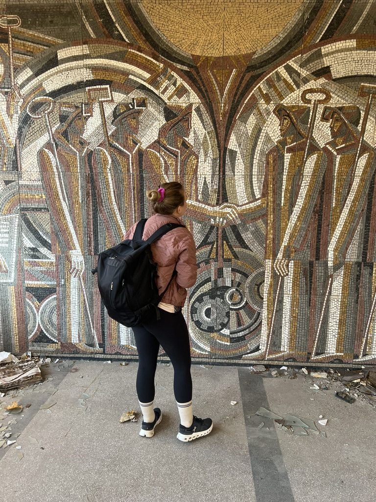 An explorer in front of a socialist-era mosaic of workers