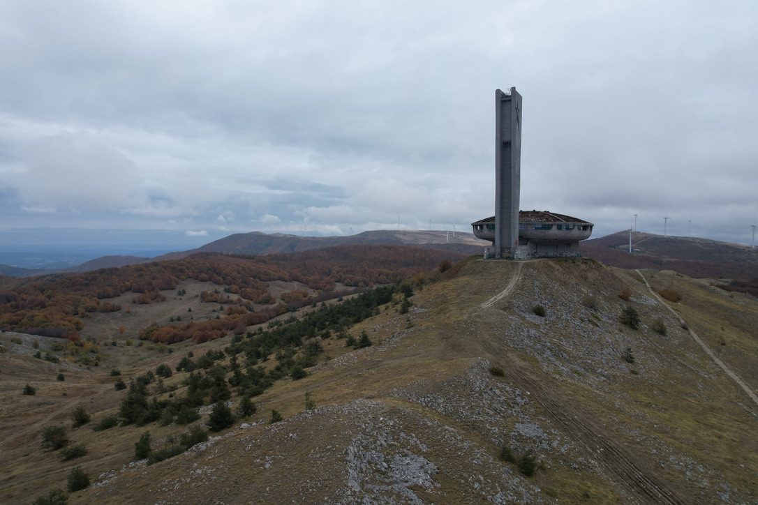 Buzludzha on its ridge under grey cloud, wind turbines on the horizon