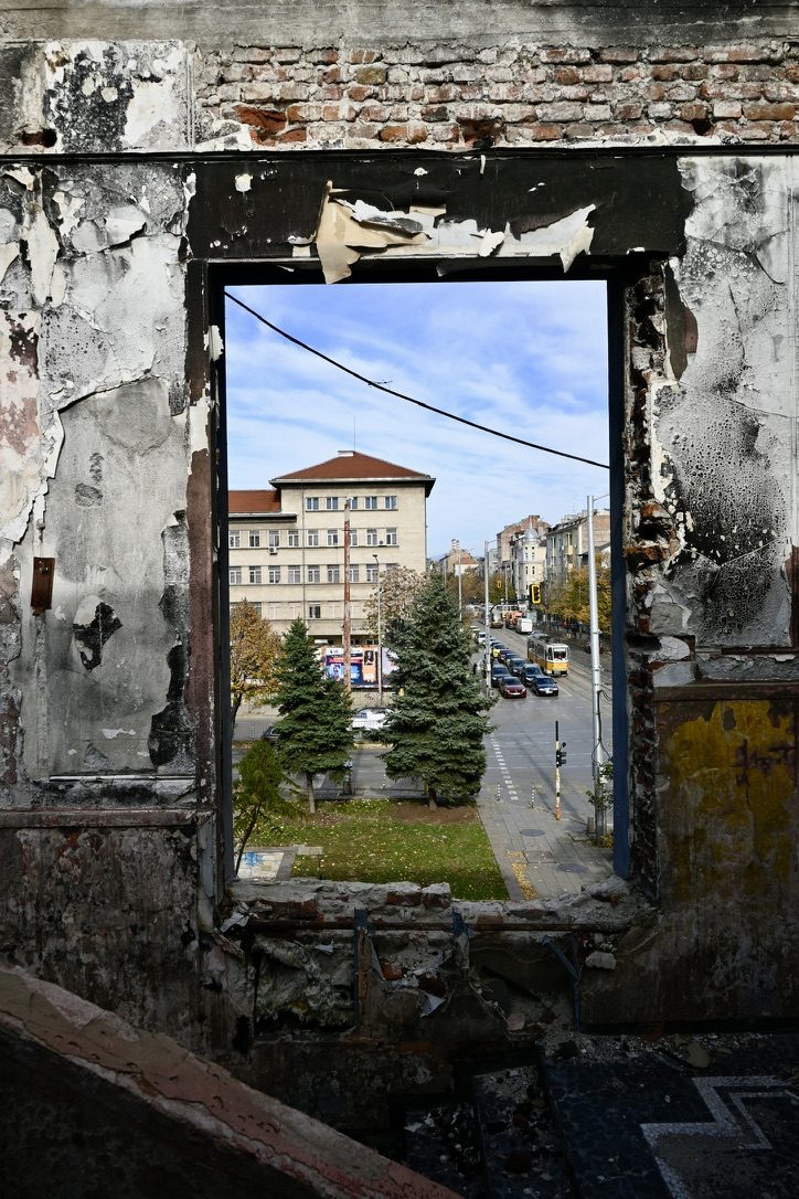 A glassless window frame looking out from a ruin onto a city street