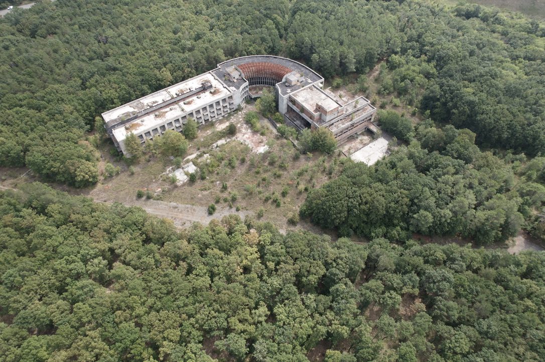 A curved concrete complex surrounded by forest, seen from the air