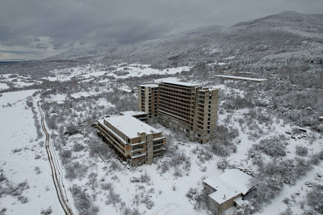 An unfinished concrete hotel in a snowy valley, seen from the air